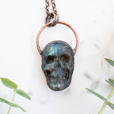 Labradorite carved skull pendant arrange beside eucalyptus branches.