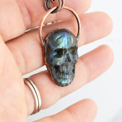 Blue, green and black Labradorite carved skull pendant in human hand.