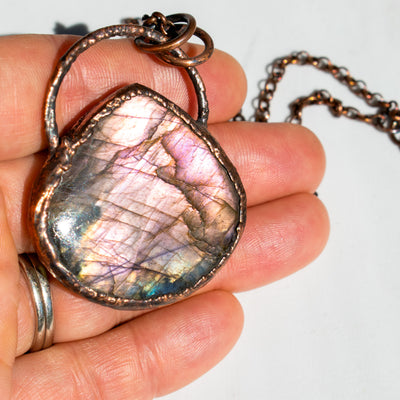 Purple and pink flashes of a Labradorite and copper necklace in human hand.