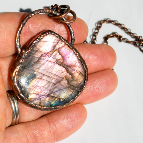 Purple and pink flashes of a Labradorite and copper necklace in human hand.