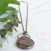 Angled photo of a Labradorite and copper necklace beside green leaves.