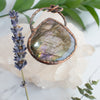 Flashes of purples in a Labradorite and Copper necklace shown beside a lavender sprig and green leaves.