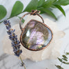 Purple and rainbow Labradorite and copper necklace beside lavender sprig and green leaves.