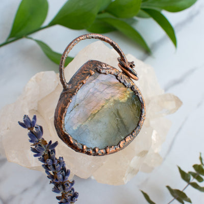 Back side angle of a Rainbow Labradorite and Copper necklace. Green leaves, eucalyptus and lavender shown beside.