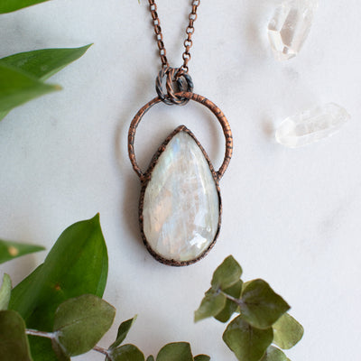 Large Rainbow Moonstone and Copper healing necklace shown beside quartz crystals and greenery.