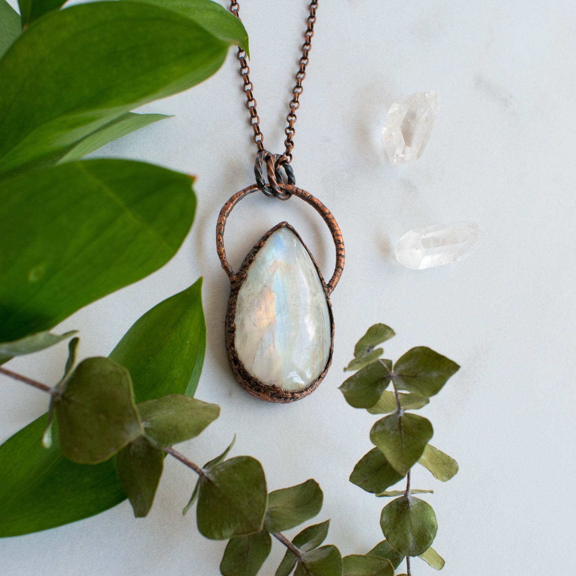 Large Rainbow Moonstone and Copper healing necklace shown beside quartz crystals and greenery.