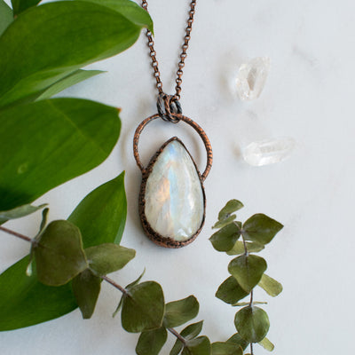 Large Rainbow Moonstone and Copper healing necklace shown beside quartz crystals and greenery.