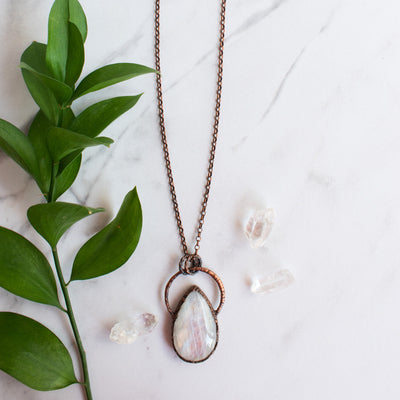 Large Rainbow Moonstone and Copper healing necklace shown beside quartz crystals and greenery.