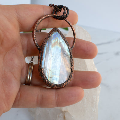 Beautiful flashes of Rainbow Moonstone shown in a hand, textured copper accents the stone.