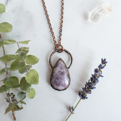 Lepidolite and Copper electroformed necklace shown beside green eucalyptus branch, quartz crystal and lavender.