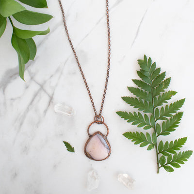 Australian Pink Opal and Copper necklace shown beside greenery and Quartz crystals.