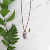 Lepidolite and Copper electroformed necklace shown beside greenery and Quartz crystals.