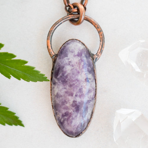 Purple Lepidolite and Copper pendant shown beside greenery and Quartz crystals.