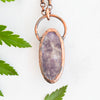 Back side of Lepidolite and Copper pendant shown beside green ferns.