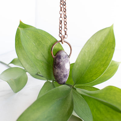 Purple Lepidolite and Copper electroformed necklace shown in front of green leaves,