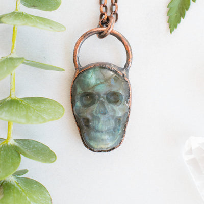 Labradorite and copper skull necklace shown beside eucalyptus branch.