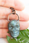 Labradorite and Copper skull necklace shown in hand with green leaves.