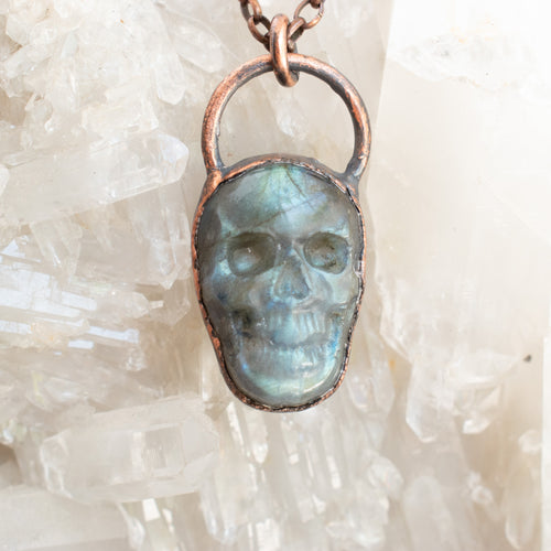 Stunning blue and green Labradorite and Copper electroformed skull pendant shown against a Quartz cluster.