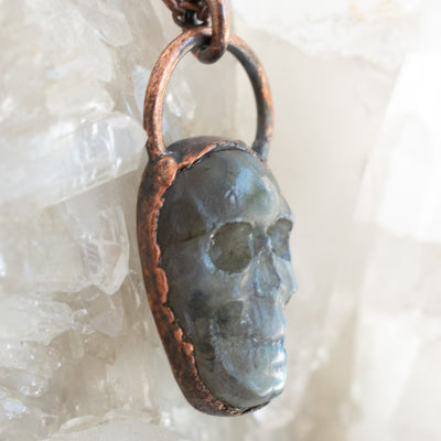 Side details of a Labradorite and Copper electroformed skull pendant shown against a Quartz cluster.