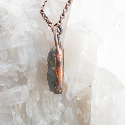 Side details of a Labradorite and Copper electroformed skull pendant shown against a Quartz cluster.