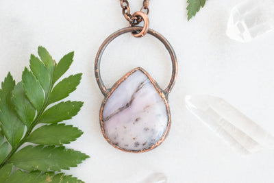 Soothing Pink Australian Opal and copper pendant shown beside green leaves Quartz crystal points.