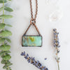 Blue green and brown swirls in a rectangular Peruvian Blue Opal and Copper necklace. Green eucalyptus and lavender and Quartz crystals are arranged beside.