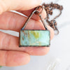 Blue green and brown swirls in a rectangular Blue Opal and Copper necklace shown held in a hand.