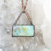 Blue green and brown swirls in a rectangular Blue Opal and Copper pendant shown in front of a Quartz cluster.