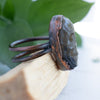 The side view shows the details on this Labradorite and Copper Skull ring shown on Palo Santo with green leaves in behind.