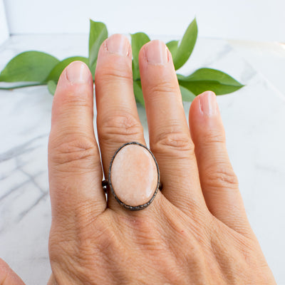 A shimmering Peach Moonstone and Copper ring worn on a hand.