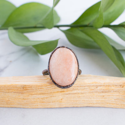 A Peach Moonstone and Copper on a stick of Palo Santo with green leaves in the background.