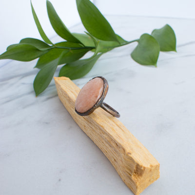 Side view of a Peach Moonstone and Copper on a stick of Palo Santo with green leaves in the background.