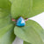 Facets on this Blue Apatite and Copper ring reflect the light with green leaves in the back ground.