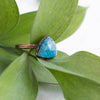 Facets on this Blue Apatite and Copper ring reflect the light with green leaves in the back ground. The side angle shows texture on the pure copper ring band.