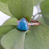 Facets on this Blue Apatite and Copper ring reflect the light with green leaves in the back ground. The side angle shows texture on the pure copper ring band.