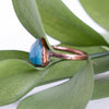 Facets on this Blue Apatite and Copper ring reflect the light with green leaves in the back ground. The side angle shows texture on the pure copper ring band.