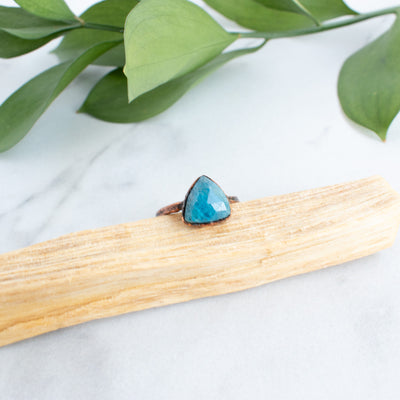 Blue Apatite and Copper electroformed ring on a stick of Palo Santo with green leaves in behind.