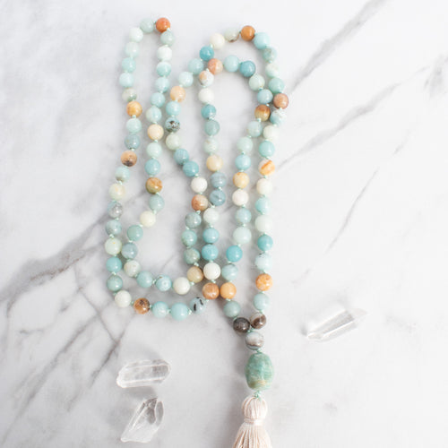 Soothing tones of blue, cream and brown blend in this hand knotted Amazonite Mala necklace, arranged beside Quartz crystals.