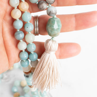 Amazonite Mala necklace with cream silk tassel held in a hand.