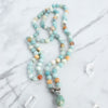 Soothing tones of blue, cream and brown blend in this hand knotted Amazonite Mala necklace, arranged beside Quartz crystals.