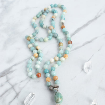 Soothing tones of blue, cream and brown blend in this hand knotted Amazonite Mala necklace, arranged beside Quartz crystals.