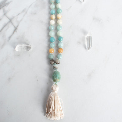 Soothing tones of blue, cream and brown blend in this hand knotted Amazonite Mala necklace, arranged beside Quartz crystals.