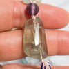 Details of the Rainbow Flourite Guru bead can be seen held in a woman's hand.