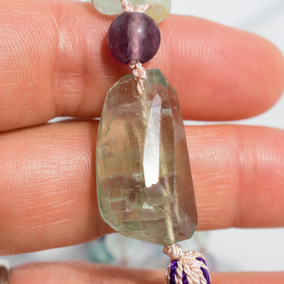 Details of the Rainbow Flourite Guru bead can be seen held in a woman's hand.