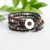 Beautiful earth tones and brown leather of the African Turquoise wrap bracelet with silver toned button shown against green leaves.