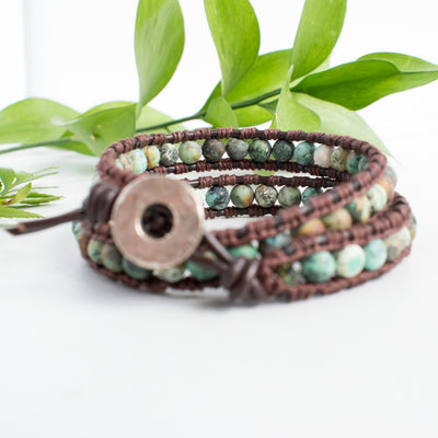 Beautiful earth tones and brown leather of the African Turquoise wrap bracelet shown against green leaves.