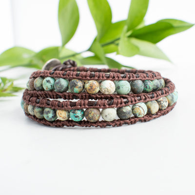 Beautiful earth tones and brown leather of the African Turquoise wrap bracelet shown against green leaves.