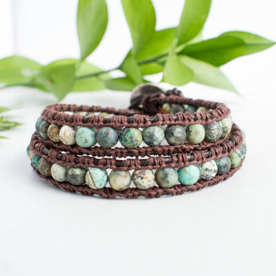 Beautiful earth tones and brown leather of the African Turquoise wrap bracelet shown against green leaves.