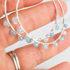 Light reflecting off the facets of blue Aquamarine beads and Silver plated Hoop earrings shown held in a woman's hand.