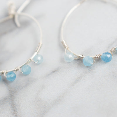 Light reflects off the facets on these blue Aquamarine silver plated hoop earrings.